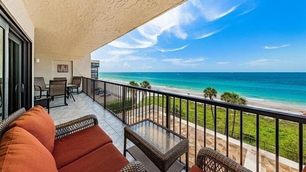 A balcony with a view of the ocean, wicker furniture, and a glass table. - Panoramic Gulf Views at Ocean Sands in Madeira Beach~ OS502 (Madeira Beach)