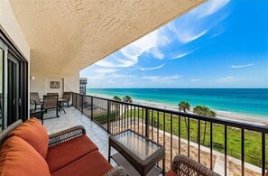 Ein Balkon mit Blick auf das Meer, ausgestattet mit Korbmöbeln und einem Glastisch.