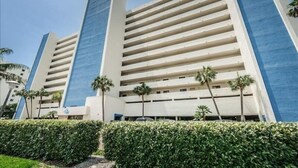 A multi-story hotel with a modern design, featuring a prominent blue and beige color scheme, and surrounded by well-maintained greenery. - Panoramic Gulf Views at Ocean Sands in Madeira Beach~ OS502 (Madeira Beach)