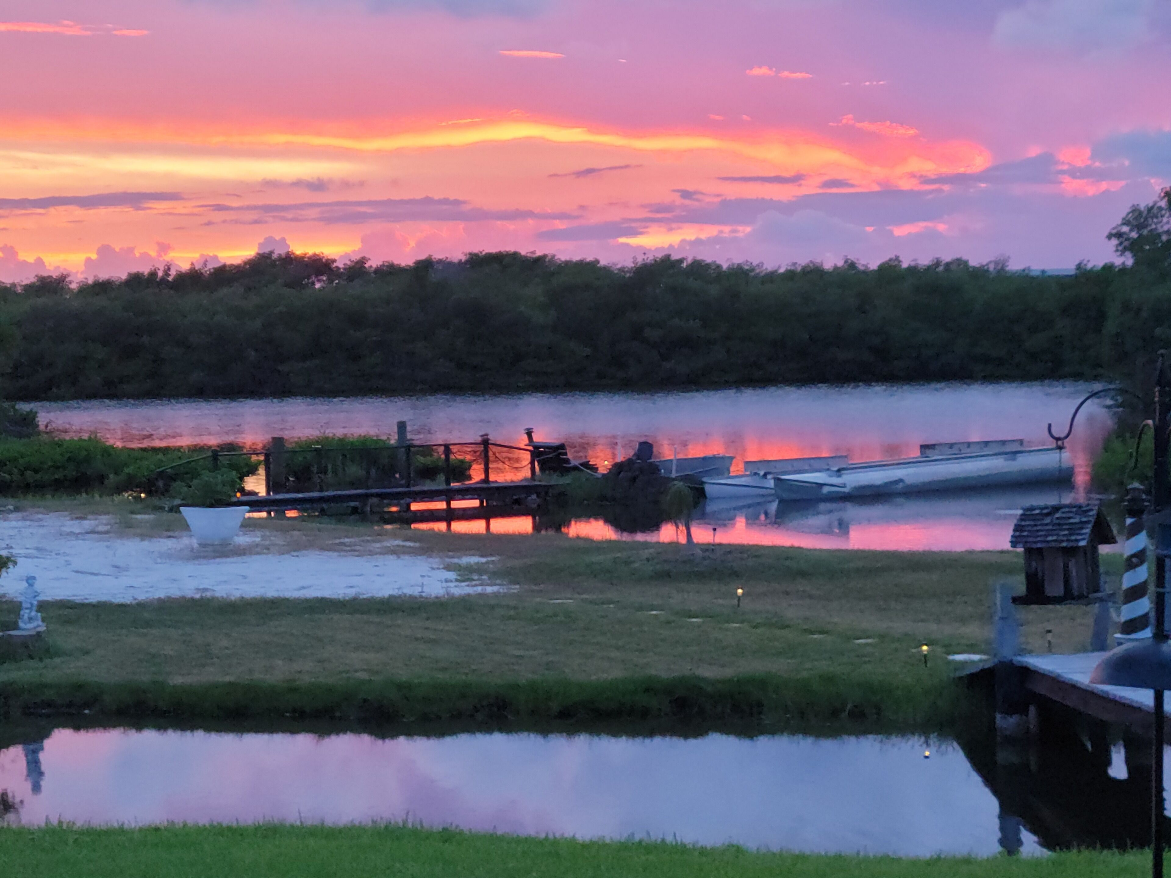 Vista de un lago con barcos amarrados, una zona verde y un muelle de madera.