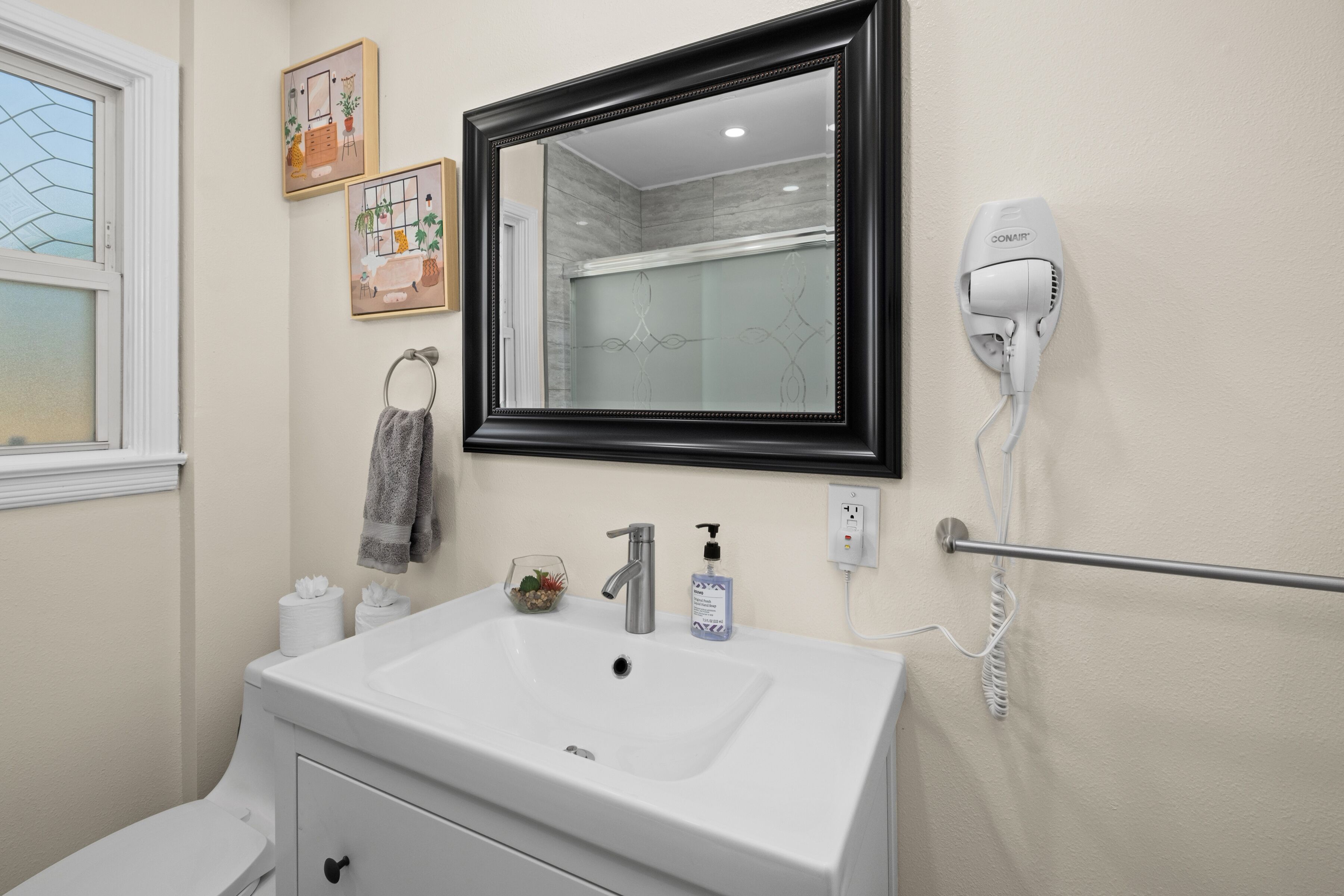 A bathroom with a white sink, a black-framed mirror, a hair dryer, and a towel rack.