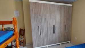 A room with a wardrobe, a bed, and a chair. - Brisas do Farol - Aluguel Economico (Arraial do Cabo)