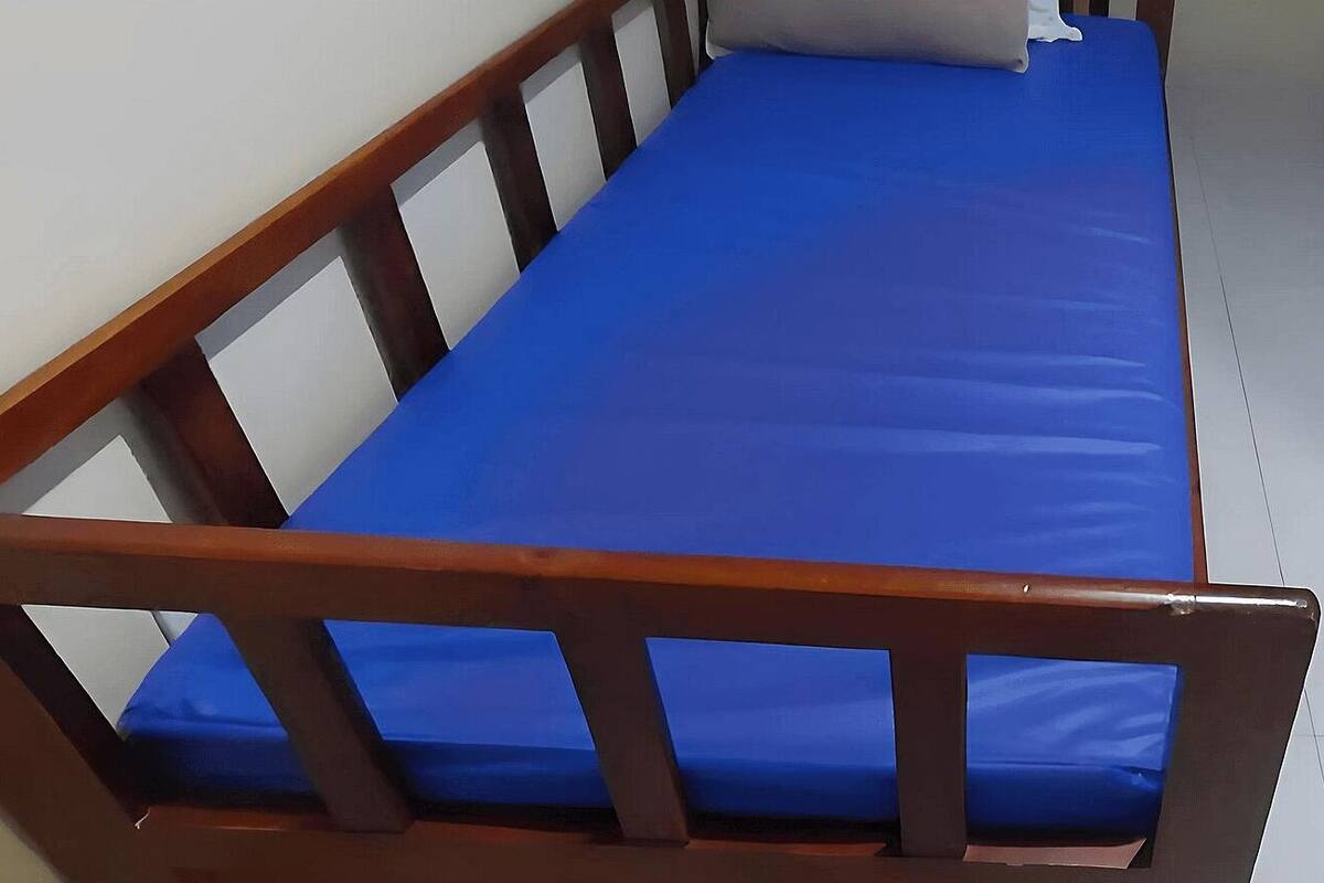 Ein kleines Zimmer mit einem Einzelbett, einem Holz-Kopfstück und einer blauen Matratze.