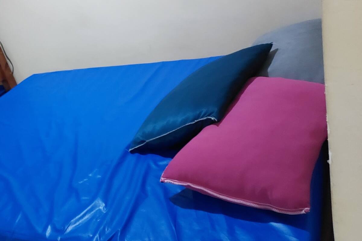 Ein Zimmer mit zwei Holzkohlschränken, jeder mit einer blauen Matratze. Im oberen Bett befinden sich drei Kissen: ein dunkelblaues, ein pinkes und ein graues.