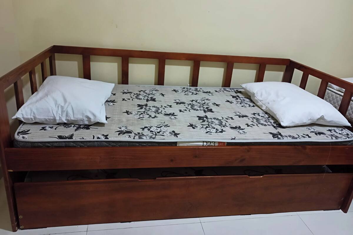 Ein hölzernes Bett mit einem blumengemusterten Matratzenüberzug, zwei weißen Kissen und einem Holz-Kopfstück.