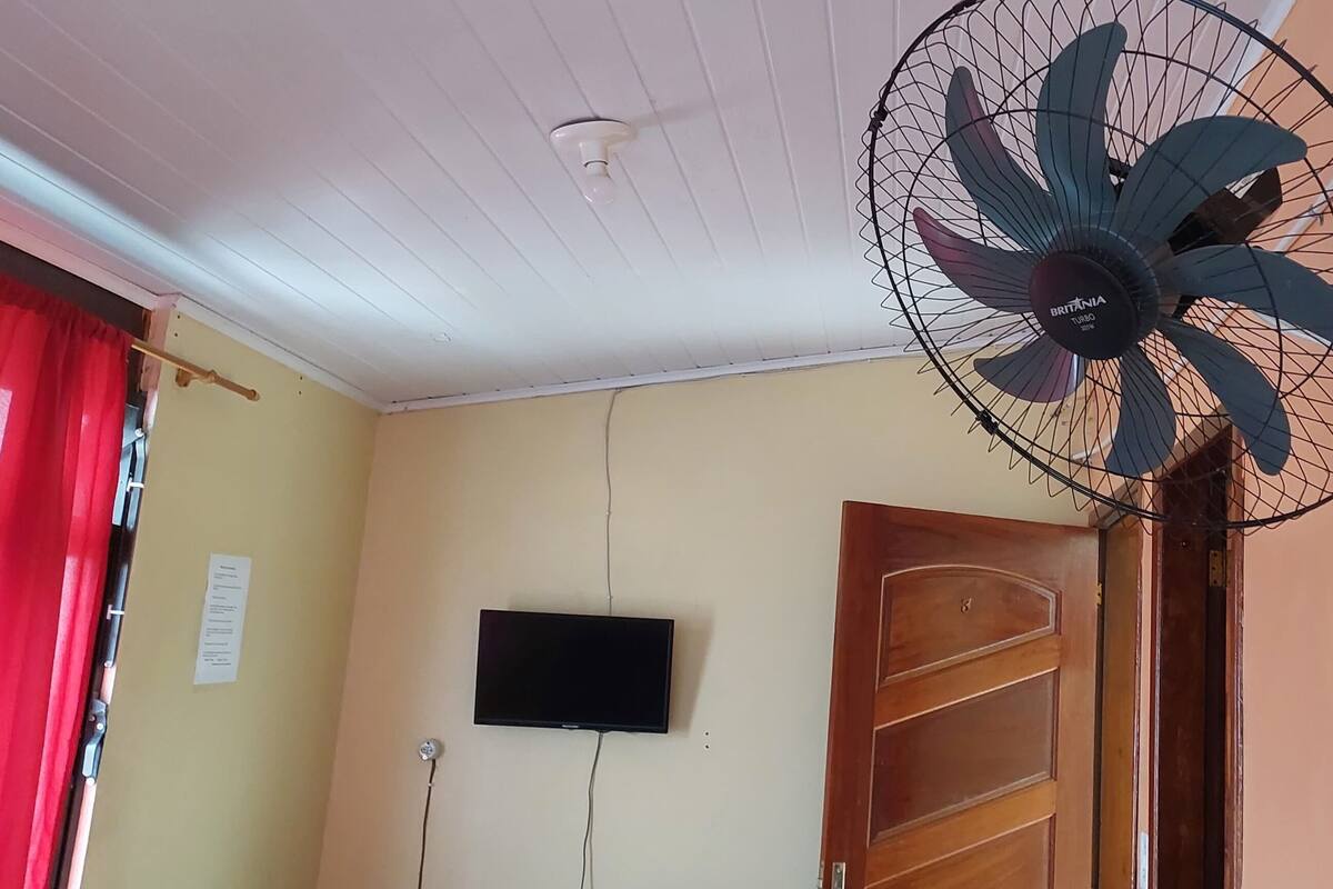 Ein Zimmer mit Deckenventilator, Wandfernseher und Holztür.