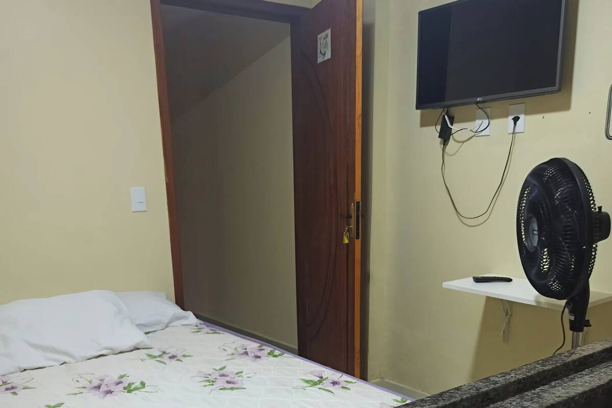 Ein Zimmer mit einem Bett, einem Schreibtisch mit Spüle, einem Fernseher und einer Tür.