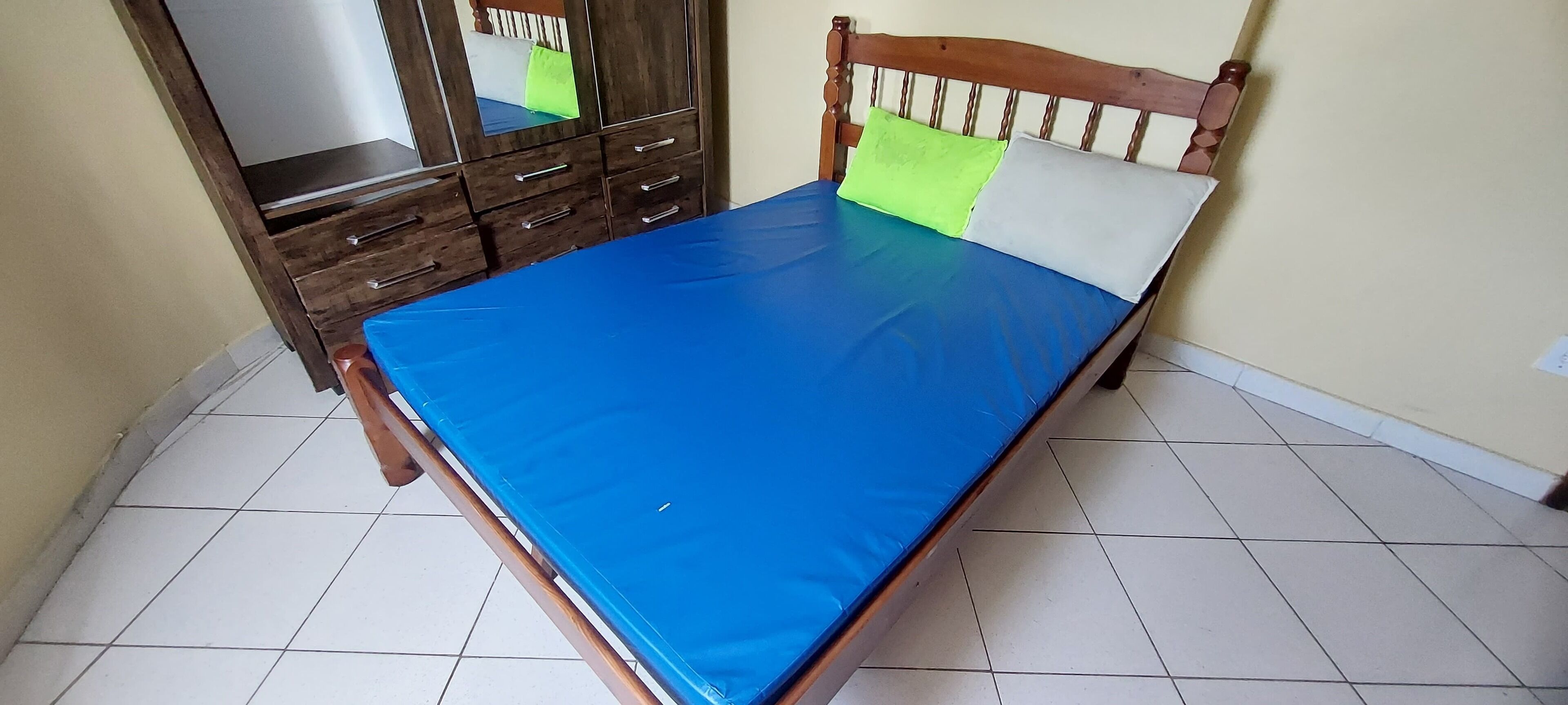 Een slaapkamer met een houten bedframe, een blauw matras en een spiegelkast.