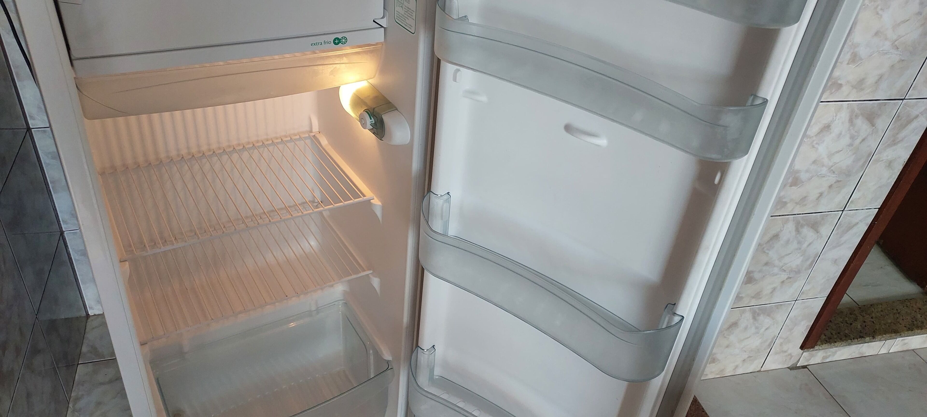Un refrigerador abierto con dispensador de agua y hielo, un compartimento congelador y un estante de vidrio.