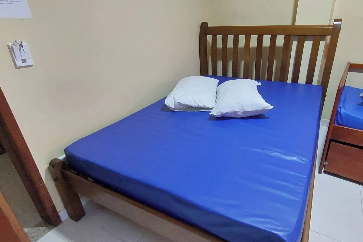Ein Zimmer mit einem Einzelbett, einem Holz-Kopfteil, einer blauen Matratze und zwei Kissen.