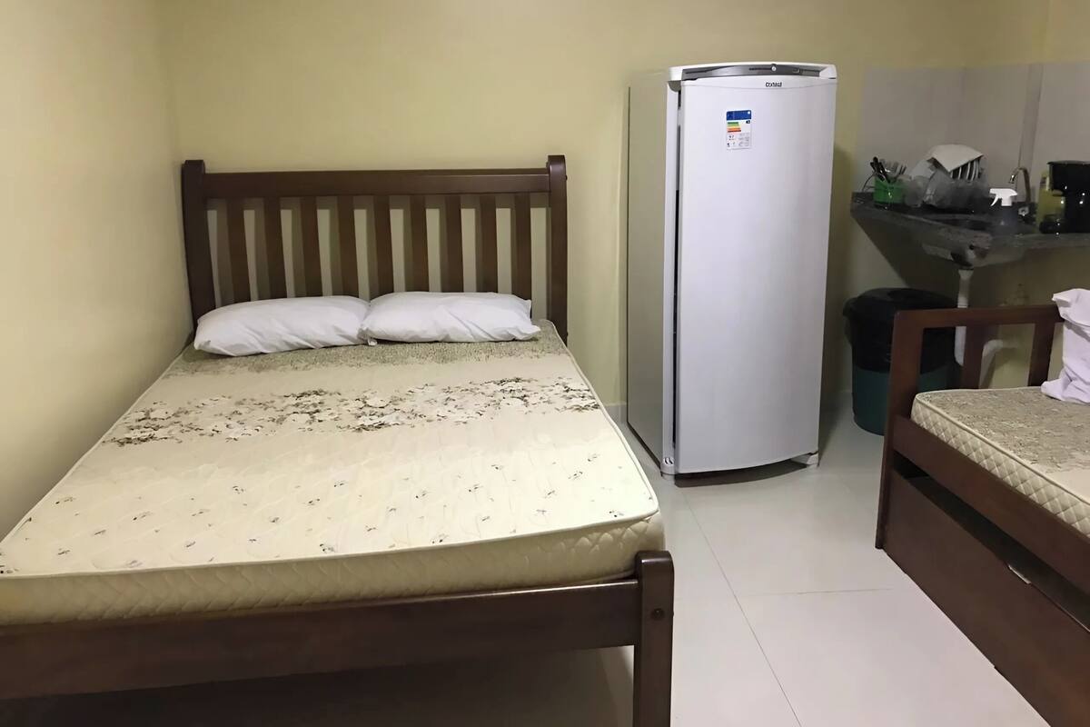 Ein kleiner, kompakter Raum mit einem Bett, einem Kühlschrank, einem Stuhl und einem Waschbecken.