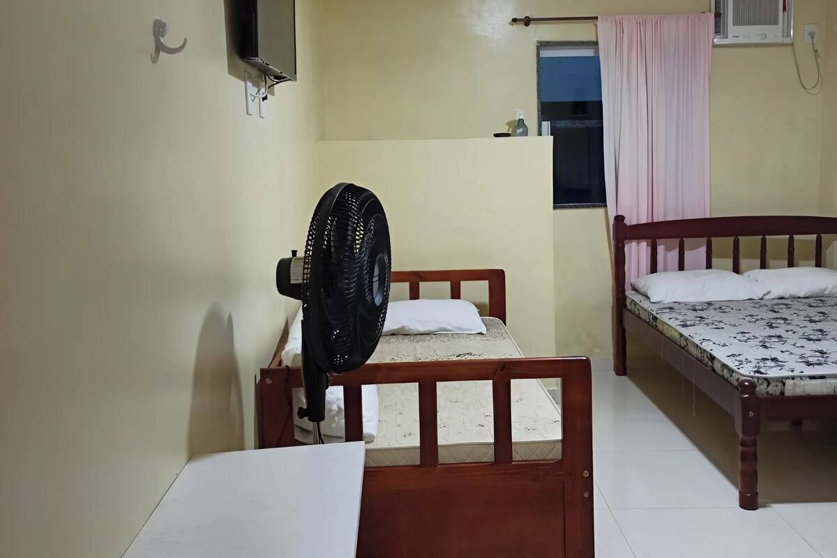 Ein Zimmer mit zwei Holzbetten, einem kleinen Tisch, einem an der Wand montierten Fernseher und einer Klimaanlage.