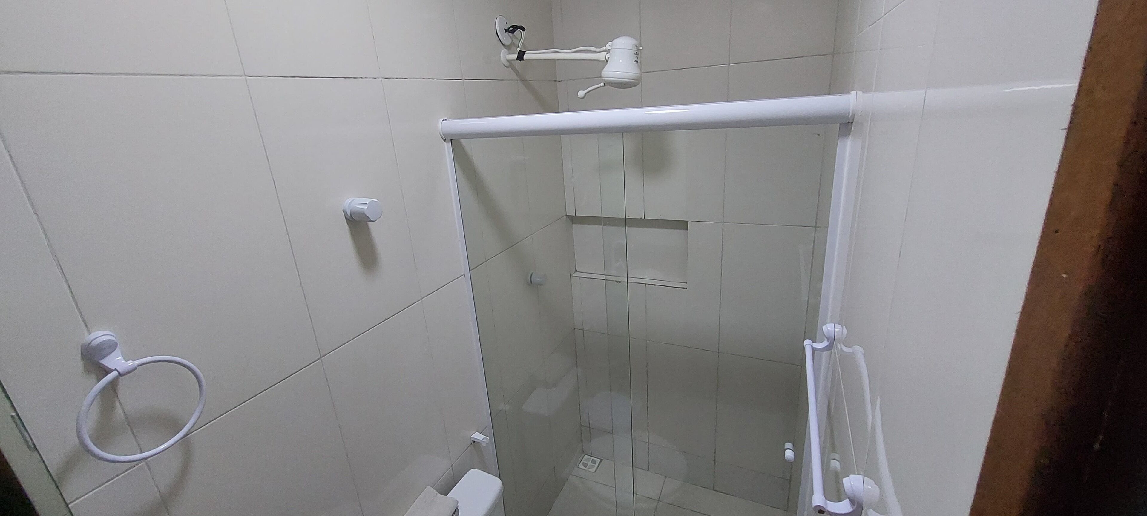 A glass-enclosed shower stall with a white towel ring, a white towel rack, and a white showerhead mounted on the wall.