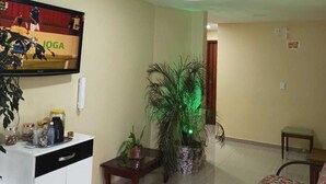 A living room with a flat-screen TV, a white cabinet, a wooden coffee table, a patterned armchair, and a potted plant. - Brisas do Farol - Aluguel Economico (Arraial do Cabo)
