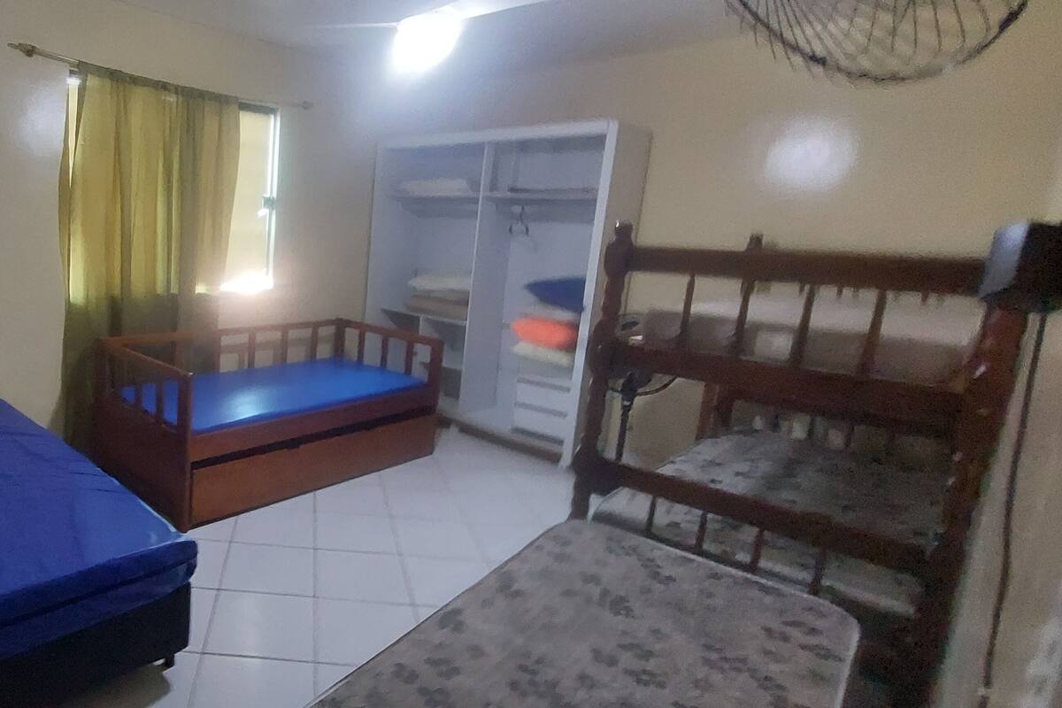 Ein Schlafraum mit Etagenbett, einem Einzelbett, einem Kleiderschrank und einem Fenster mit Vorhängen.