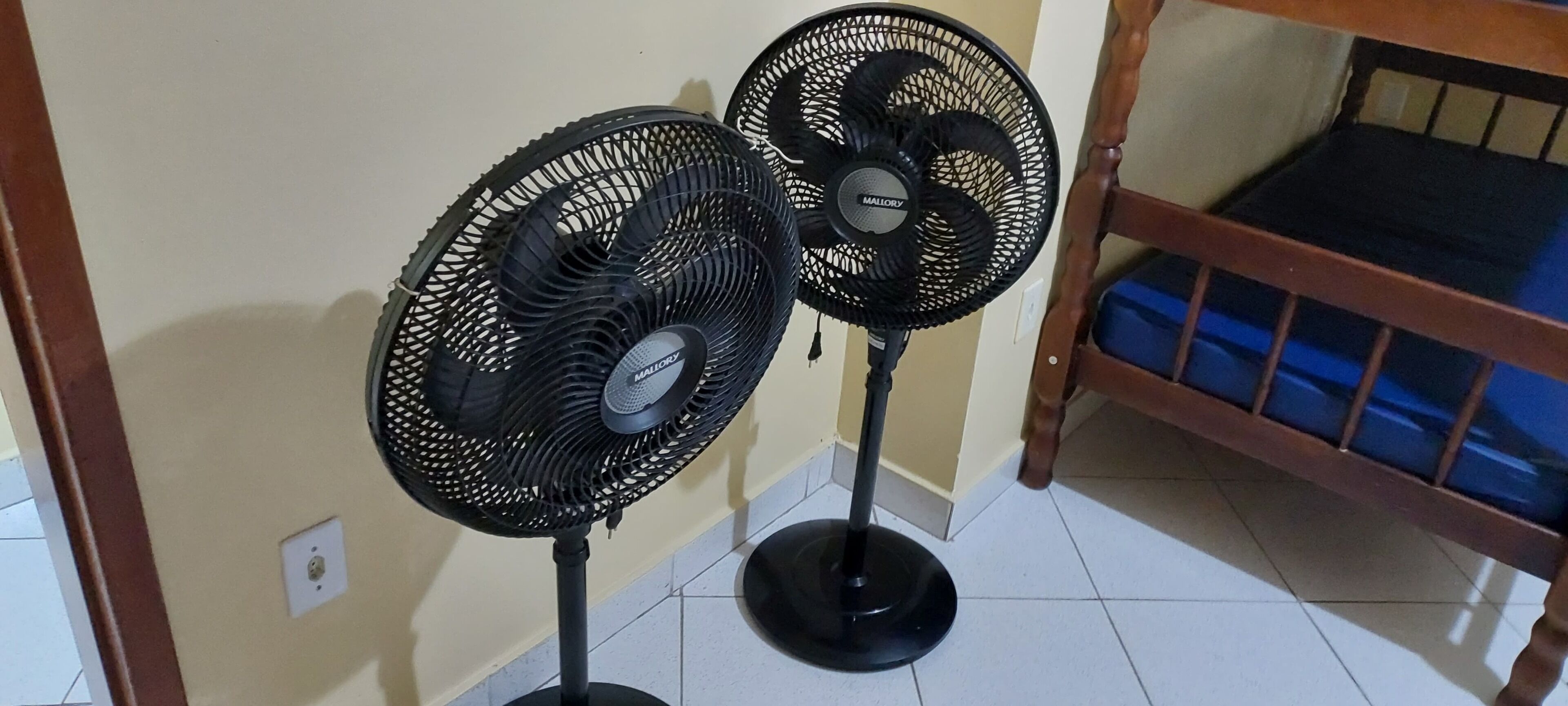 Two standing fans in a room with a wooden bunk bed and a tiled floor.