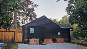 A black wooden building with a sloped roof, a small window with a decorative sticker, and wooden planters with plants.