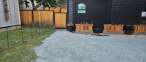 A gravel driveway leading to a black building with a wooden fence and wooden planters.