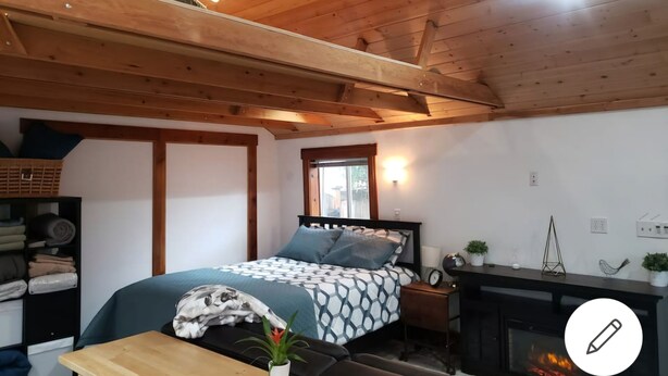 A cozy bedroom with a bed, a wooden ceiling, a fireplace, and a window.