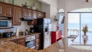 A modern kitchen with granite countertops, stainless steel appliances, and wooden cabinets. - Sunset 303 - Ocean View 3 BR Condo (Potrero)