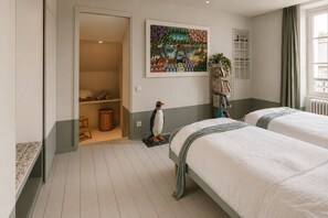 A hotel room with two beds, a wardrobe, a painting, and a small penguin figurine.