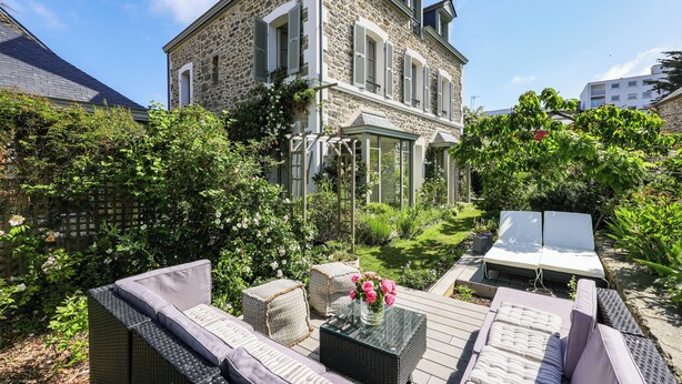 A stone building with a conservatory, outdoor seating, and lush garden.