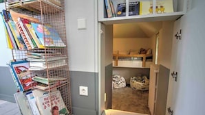 A room with a bunk bed, a bookshelf filled with books, and a small storage area with bags.