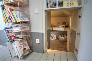 Une chambre avec un lit superposé, une bibliothèque remplie de livres et un petit espace de rangement avec des sacs.