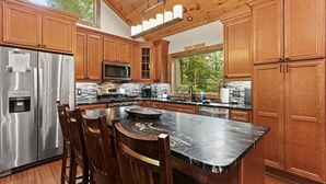 Una cocina moderna con armarios de madera, electrodomésticos de acero inoxidable, una isla grande con taburetes y vistas a zonas verdes.