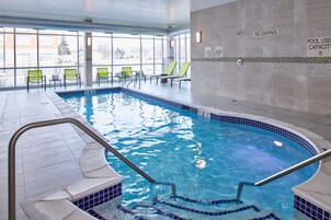 Una piscina interior con agua cristalina, un trampolín y sillas de descanso.