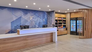 A reception area with a wooden counter, a blue wall with text, and a refrigerator stocked with beverages. - SpringHill Suites by Marriott Detroit Dearborn (Dearborn)