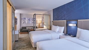 A hotel room with two beds, a sofa, a desk, a lamp, and a large mirror.