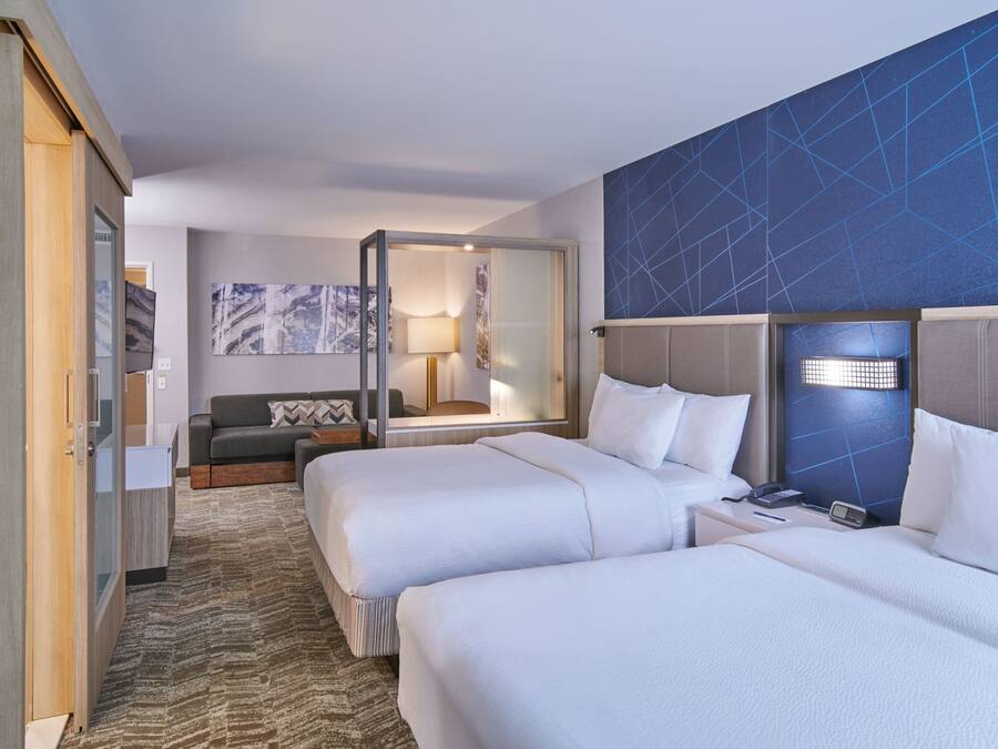 A hotel room with two beds, a sofa, a desk, a lamp, and a large mirror.