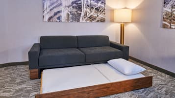 A modern room with a grey sofa, a wooden bed frame, and a patterned carpet.