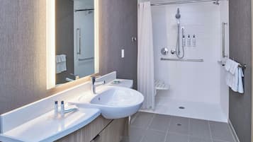 Ein modernes Badezimmer mit Waschbecken, großem Spiegel, Duschkabine und Handtuchhalter.