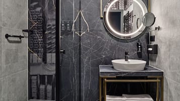 A modern bathroom with a glass-enclosed shower, a round mirror, and a white sink on a marble countertop.