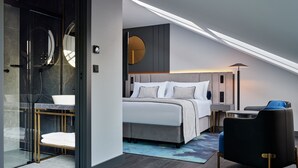 A modern hotel room with a bed, a seating area, a glass-enclosed shower, and a round mirror. - Garamond, a Tribute Portfolio Hotel, Krakow Old Town - Adults Only (Kraków)