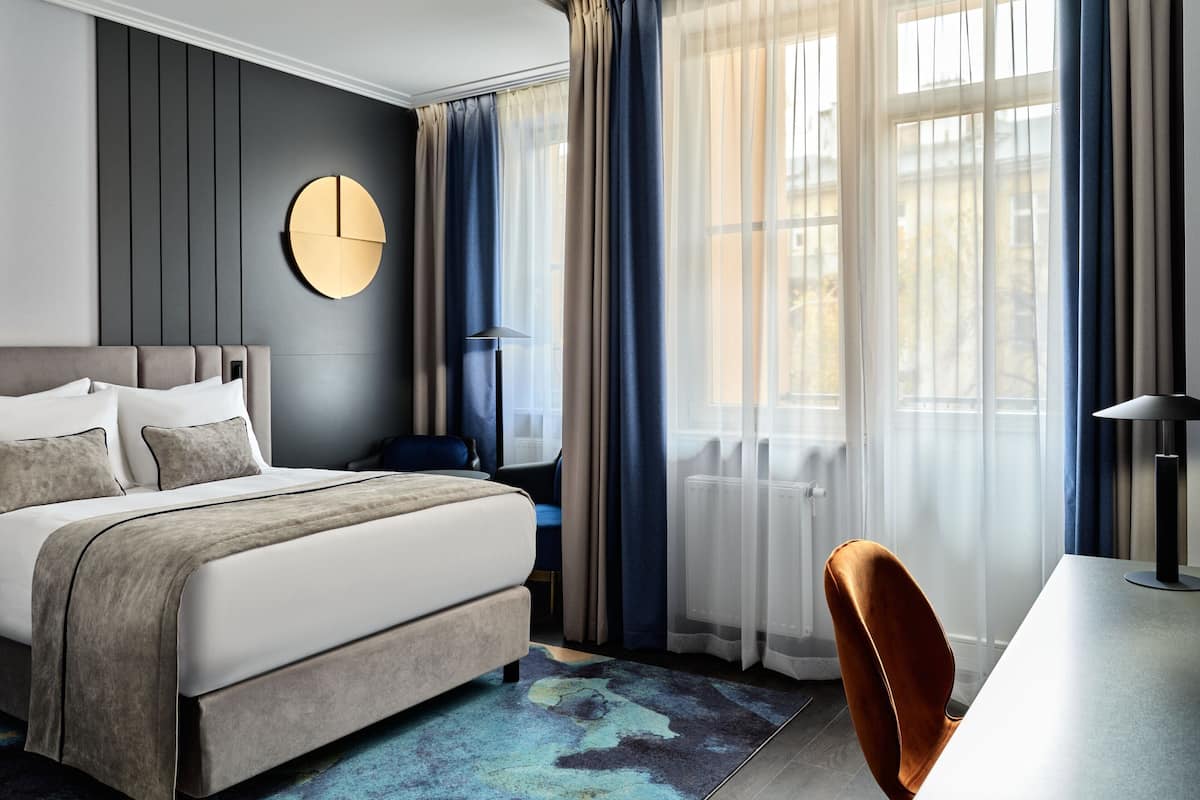 Una habitación de hotel moderna con una cama grande, un reloj de pared redondo, un escritorio y una silla.