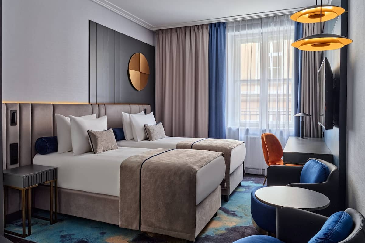 Una habitación de hotel moderna con dos camas, un escritorio, una silla y un televisor.