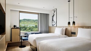 A hotel room with two beds, a TV, a small table, and a window with a view of greenery. - Fairfield by Marriott Okayama Hiruzen Highland (Maniwa)