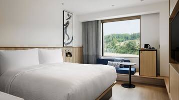 Una habitación de hotel moderna con una cama grande, una mesita pequeña, un sofá, un televisor y una ventana con vistas a un bosque.