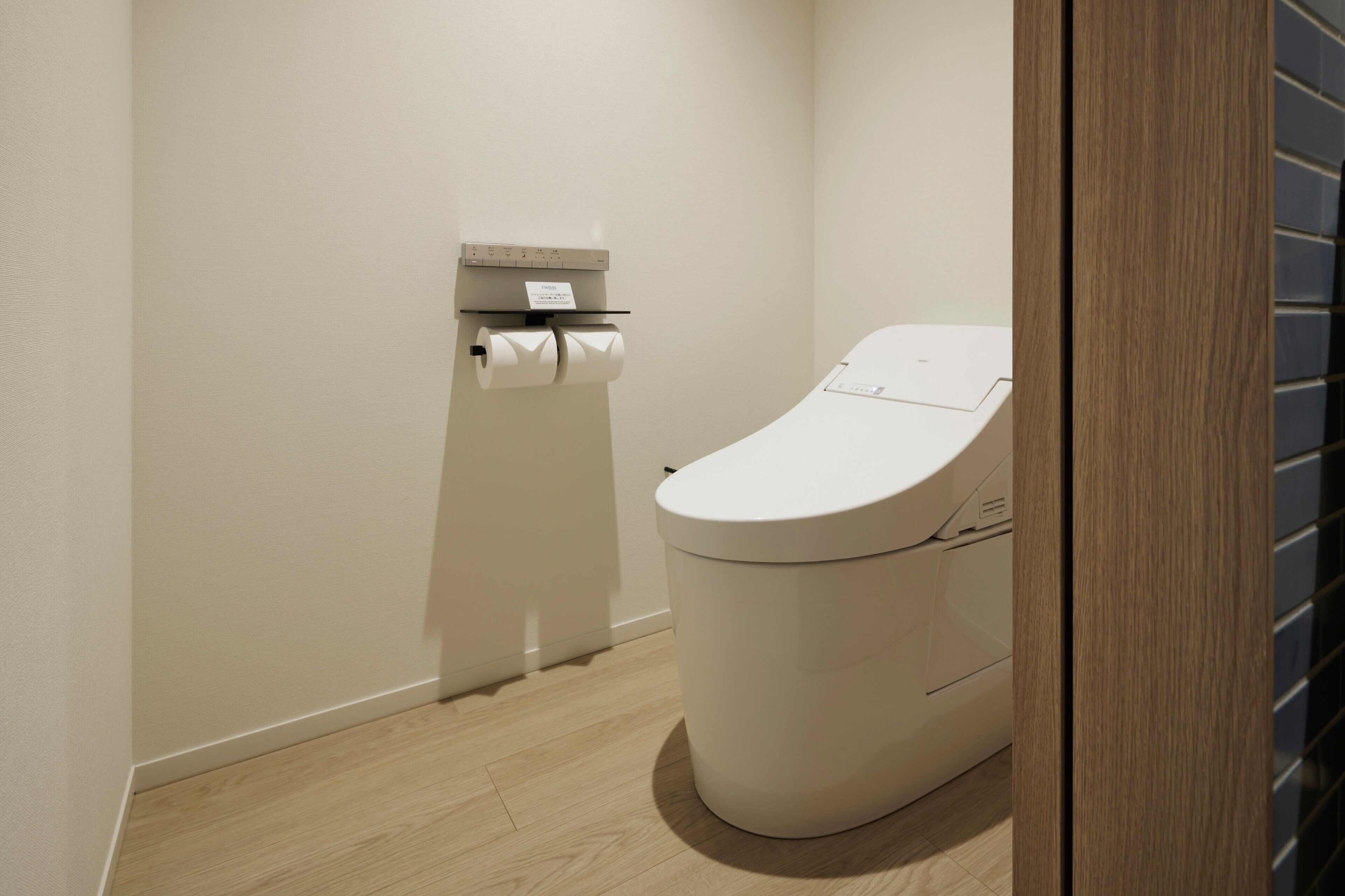 A modern bathroom with a toilet, a toilet paper holder, and a wooden floor.