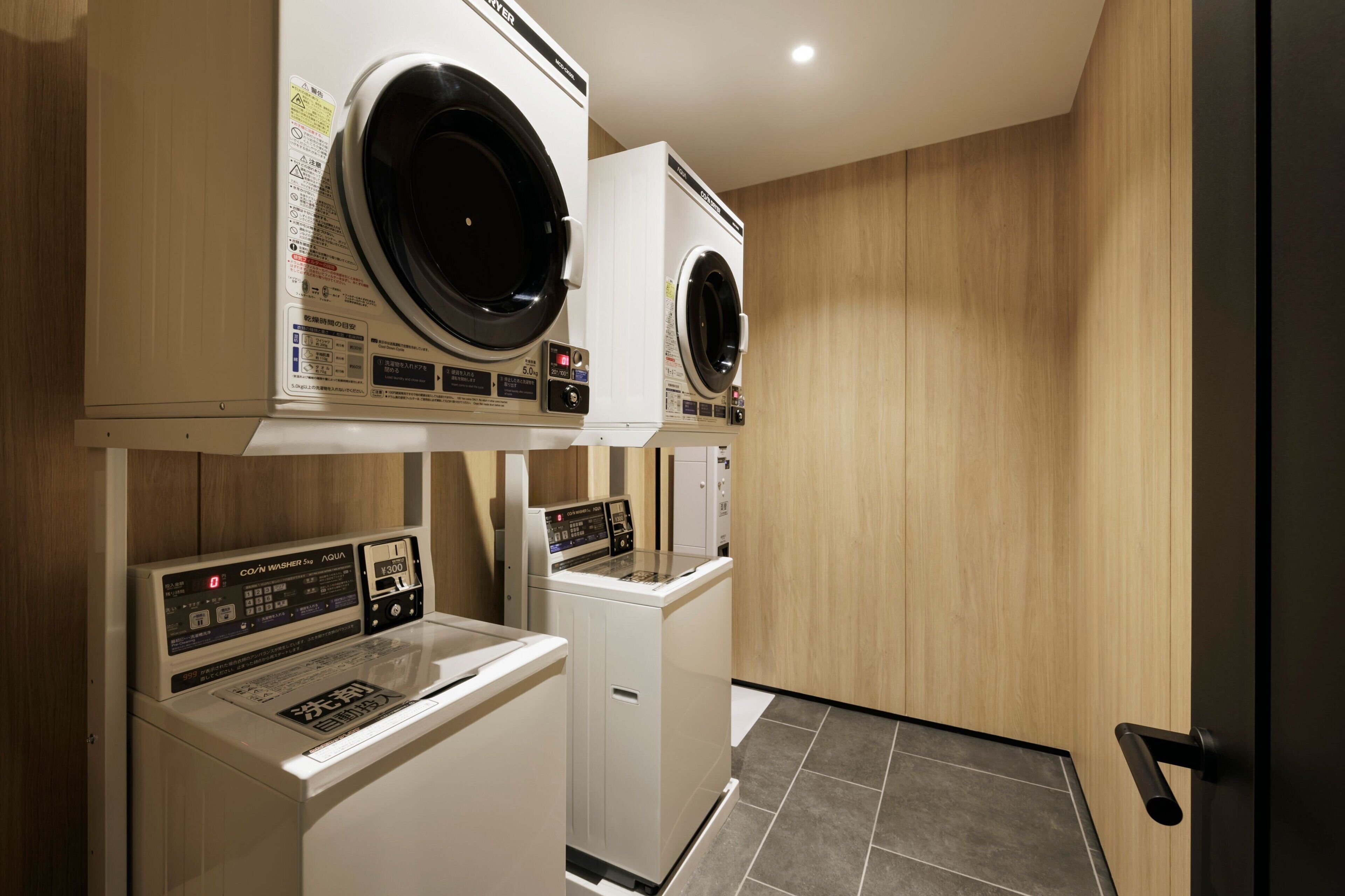 A laundry room with two front-loading washers and dryers, wooden walls, and a tiled floor.