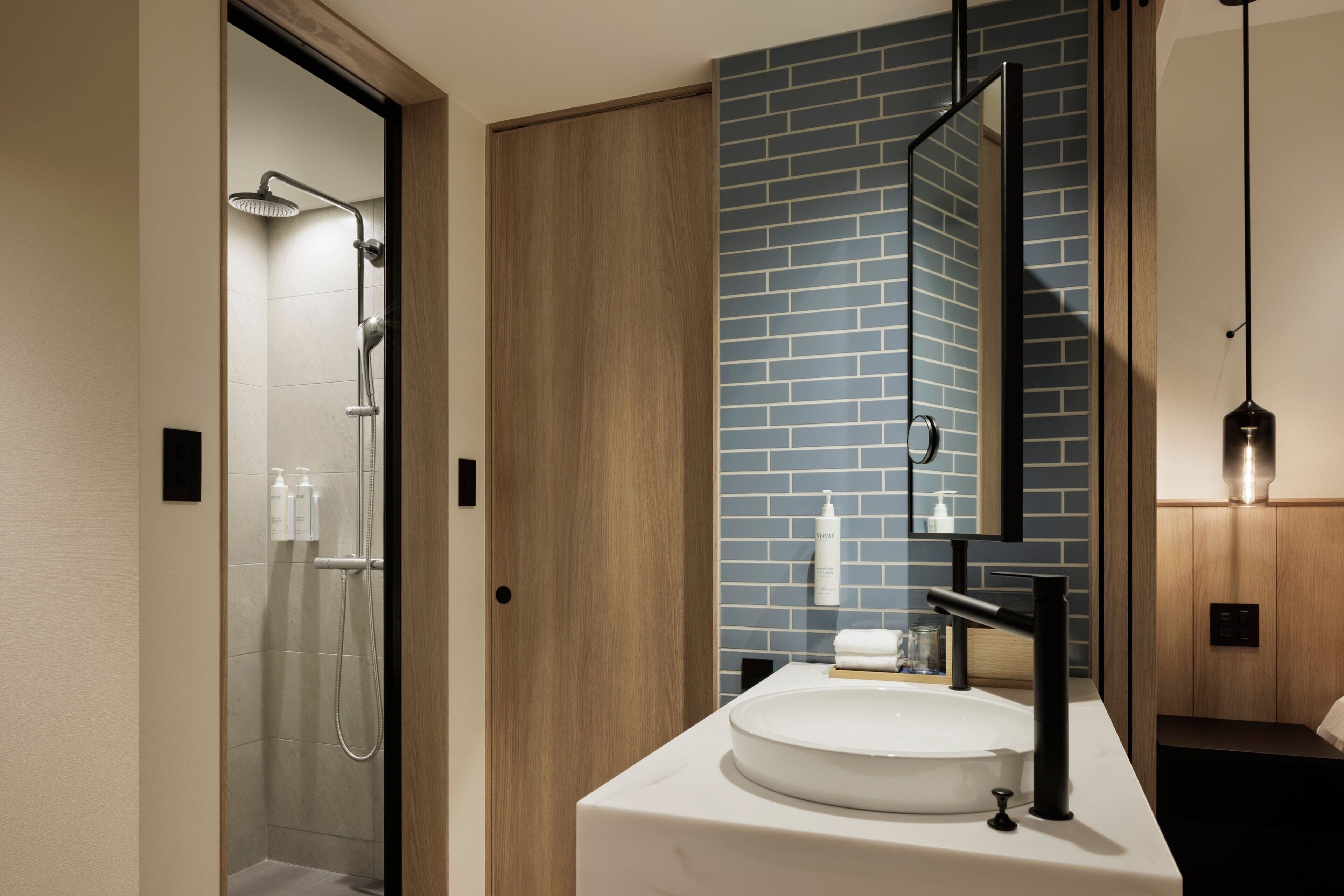 A modern bathroom with a glass shower, a white sink, and a mirror with a blue-tiled wall.