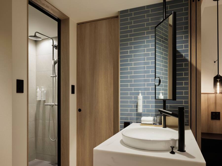 A modern bathroom with a glass shower, a white sink, and a mirror with a blue-tiled wall.