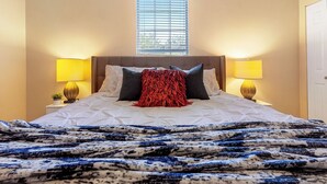 A neatly made bed with a patterned blanket, two bedside lamps, and a window with blinds.