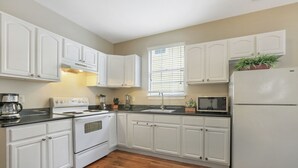 A kitchen with white cabinets, a stove, a sink, a refrigerator, and a window with blinds.