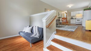 A modern living room with a grey sofa, wooden flooring, and a staircase leading to a kitchen area.