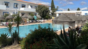 A pool area with lounge chairs, umbrellas, and a building with a tiled roof. - Best location in Lagos with superb pool area! (Lagos)
