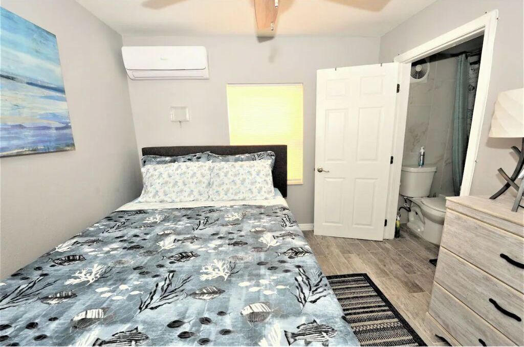 Quarto com cama, cômoda, porta e janela com persianas.